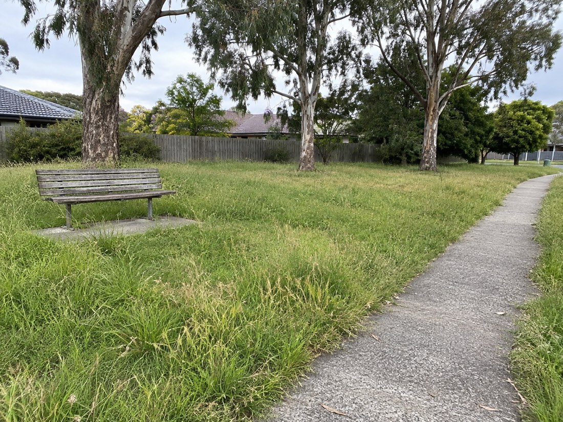 Illustrative before photo: long grass around a reserve bench and spilling onto a concrete path